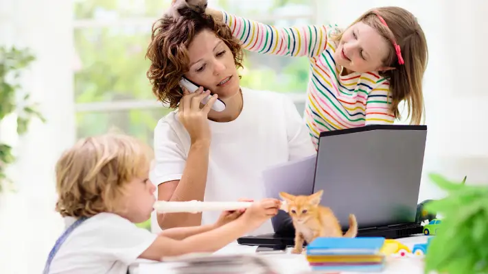 Image of one adult on a phone while two young persons playing around a table.