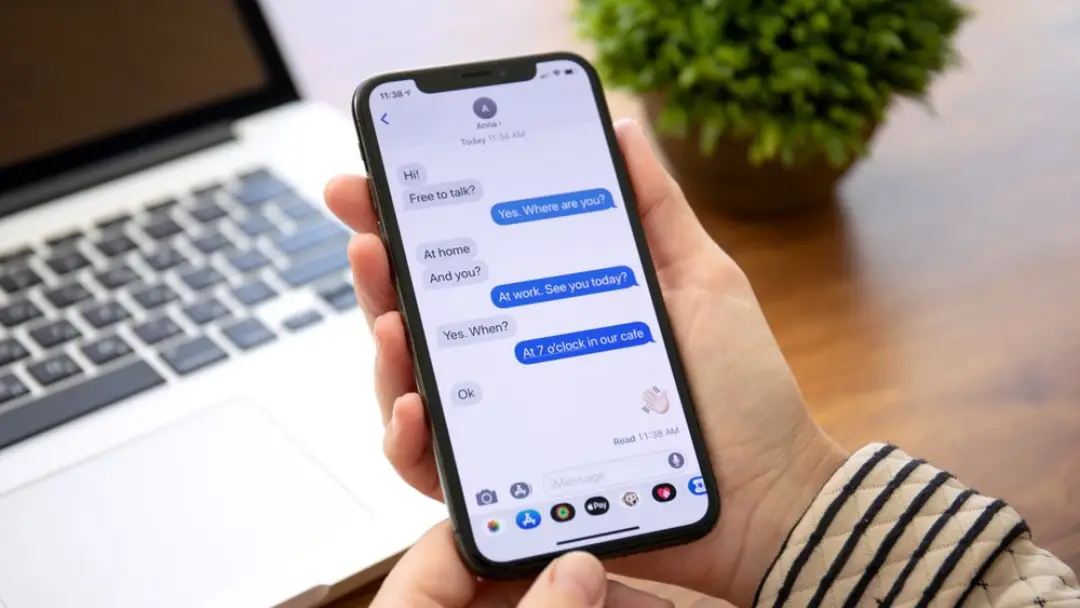 image of a person at a desk holding a mobile device, depicting work group chats.