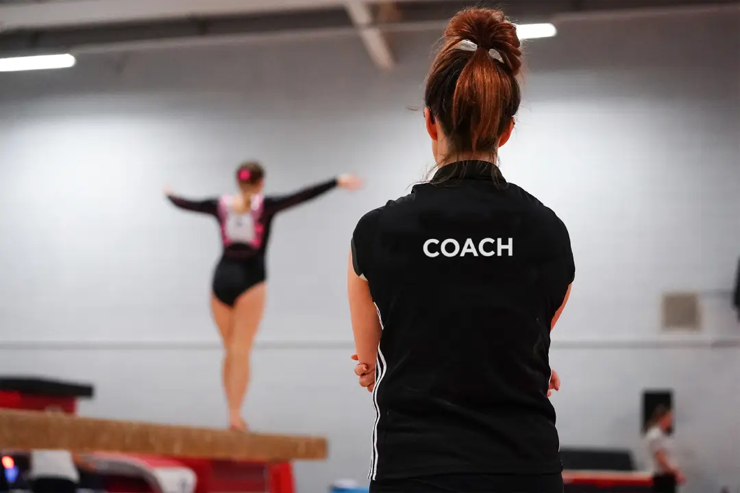 Image of a gymnast balancing on a vault with the coach observing.